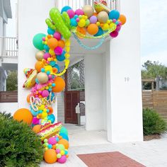 an arch made out of balloons and streamers in front of a white building with steps leading up to it