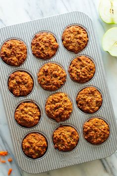 carrot muffins in a muffin tin on a marble surface with sliced apples