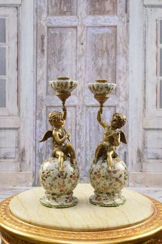 two vases sitting on top of a table with gold trimming and angel figurines