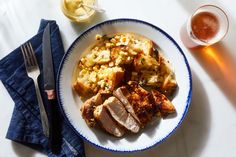 a white plate topped with meat and potatoes next to a glass of beer on top of a table