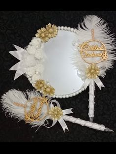 a white and gold mirror with some feathers on it's side, next to a pen