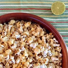 a wooden bowl filled with popcorn next to a lemon wedge on a striped table cloth