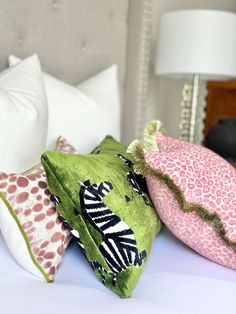 three decorative pillows on a bed with white sheets and pink, green, and black accents