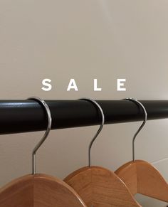 three wooden clothes hangers with the word sale written on them in white lettering, hanging from a black metal rail