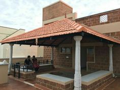 two people sitting on a bench in front of a brick building with a red roof