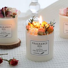 three candles with flowers in them sitting on a white table cloth next to each other