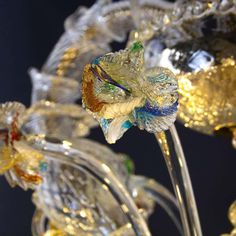 a glass flower that is sitting on a stand with gold and blue flowers in it