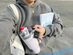 a person holding a book and a water bottle in their left hand while standing next to a parking lot