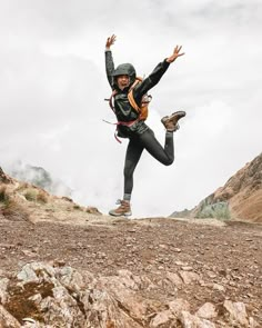 a man is jumping in the air on top of a rocky hill with his arms outstretched