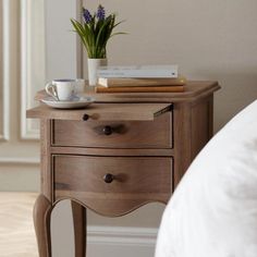 a small wooden table with some books and a coffee cup on it next to a bed