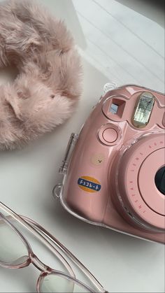 a pink polaroid camera sitting on top of a table next to some glasses and a stuffed animal