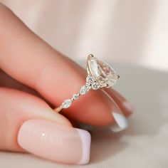 a woman's hand holding an engagement ring with a pear shaped diamond on it