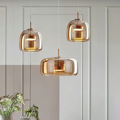 three lights hanging from the ceiling above a dining room table and chairs with flowers in vases