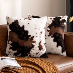 two brown and white pillows sitting on top of a leather couch next to a book