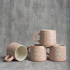 four coffee mugs sitting next to each other on a gray surface with white and pink designs