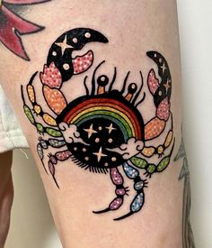 a colorful crab and rainbow tattoo on the right side of the leg, it is black with white dots