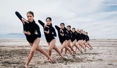 a group of women in black leotards are dancing on the beach