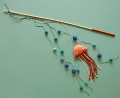 a knitting needle and some beads on a green surface with an orange fish pinion