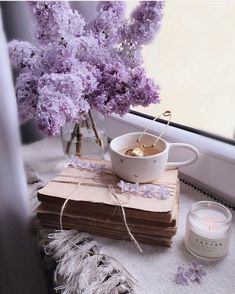 purple flowers are in a vase and on top of some books next to a candle