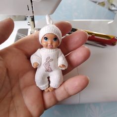 a hand holding a small doll in front of a sewing machine