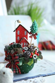 a small christmas arrangement in a bowl on a table with a teddy bear and other decorations