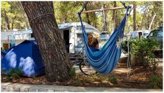 a blue hammock hanging from a tree in front of a camper trailer