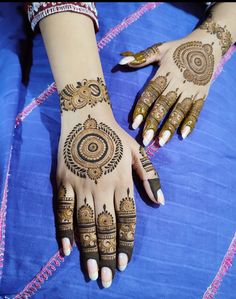 two hands with henna designs on them sitting on a blue cloth covered tablecloth