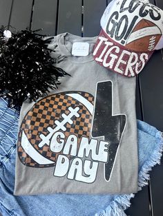 Get ready for the big game day with our Game Day Checkered Football Tee! The perfect shirt for any football fan, this tee features a fun checkered design that will make you stand out in the crowd. With its comfortable fit and stylish look, you'll be the envy of all your friends. Show off your team spirit and passion for the game in style! professionally printed tee brand: M&O Vintage Wash color: Grey comfy, unisex fit ships within 10-14 business days. Collegiate T-shirt With Sublimation Print For Game Day, Collegiate T-shirt For Game Day With Sublimation Print, Sporty Graphic Print Top For Tailgating, Sports Fan T-shirt With Team Name For Tailgating, Sports Fan Tops With Sublimation Print For Game Day, Sporty T-shirt For Game Day Football Season, Sporty T-shirt For Football Season Game Day, Sporty T-shirt For Game Day During Football Season, Team-colored T-shirt For Football Game Day