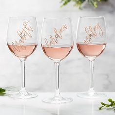 three wine glasses sitting on top of a table next to each other with gold lettering