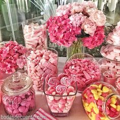 a table topped with lots of candy covered in pink and yellow candies next to vases filled with flowers