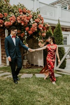 a woman in a red dress and a man in a black suit are holding hands