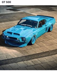 a blue muscle car parked on the side of a road next to a brick sidewalk