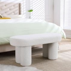 a white bed sitting next to a window with blinds on the windowsill and a footstool in front of it