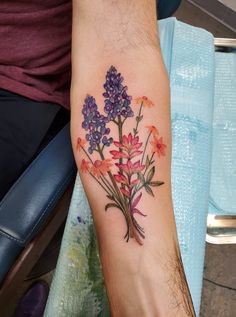 a person with a tattoo on their arm holding a bouquet of purple and orange flowers