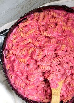 a skillet filled with macaroni and cheese being stirred by a wooden spoon