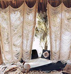 an open window with curtains and pillows on the floor in front of it, next to a potted plant