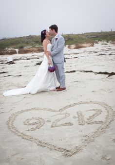 a bride and groom standing in the sand with a heart drawn in the sand on their wedding day