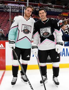 two men standing next to each other on top of an ice rink with hockey sticks