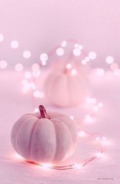 two white pumpkins sitting on top of a table next to some string lights in the background