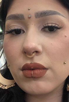 a close up of a person with makeup and piercings on her nose, wearing gold hoop earrings