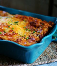 a blue casserole dish with cheese and green onions in it on a placemat