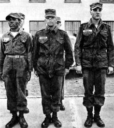 three men in uniforms standing next to each other on the street, with one man looking at the camera