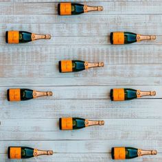 six bottles of champagne lined up on a white wooden surface with corks in the middle