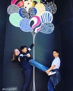 two people standing next to each other on top of a wall with balloons attached to it