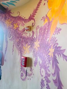 a man standing in front of a wall painted with purple and yellow flowers on it