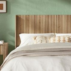 a bed with white sheets and pillows in a green room next to a wooden headboard