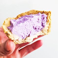 a hand holding up a half eaten cookie with purple frosting on the outside and inside