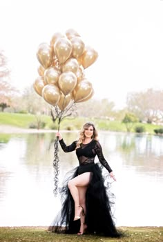 a woman in a black dress is holding some gold balloons and posing for the camera