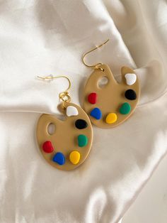 a pair of earrings with paintbrushes painted on them sitting on a white sheet