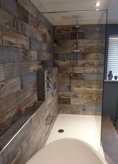 a bath tub sitting next to a wooden wall in a bathroom with a walk in shower